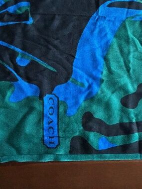 A bold Coach scarf featuring a vibrant blue and green "drip-leopard" camo print